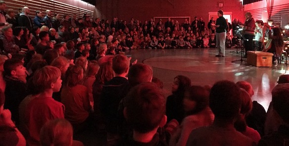 Auf dem Bild sind Lehrer, Eltern und Schüler_innen beim Weihnachtssingen in der Sporthalle zu sehen. Ein paar Kinder spielen dabei Instrumente.
