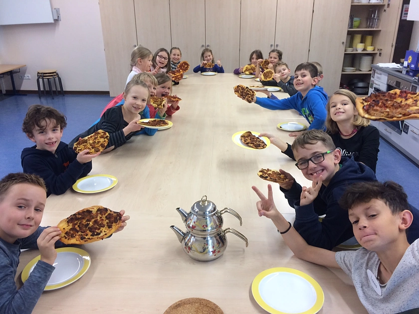 Auf dem Bild sind Schüler und Schülerinnen der Schule St. Magnus zu sehen, die eine Türkische Pizza in den Händen halten.