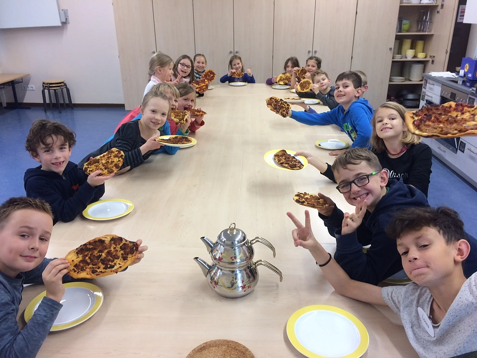 Auf dem Bild sind Sch&uuml;ler und Sch&uuml;lerinnen der Schule St. Magnus zu sehen, die eine T&uuml;rkische Pizza in den H&auml;nden halten.